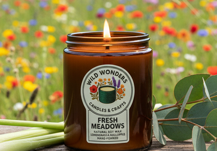Candle in a brown jar with a label on a wooden surface in front of a field of wildflowers