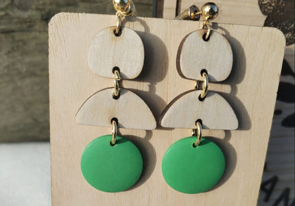 Green and beige layered earrings on a wooden display with flowers.