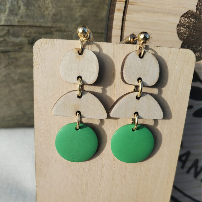 Green and beige layered earrings on a wooden display with flowers.