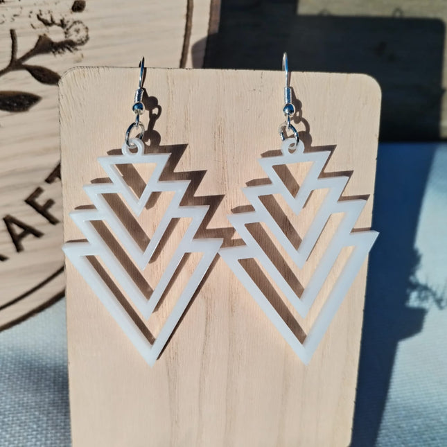 Geometric earrings on a wooden display card with a blurred background