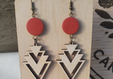 Pair of earrings with red circular tops and geometric triangle designs on a wooden card.