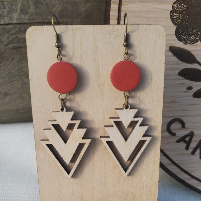 Pair of earrings with red circular tops and geometric triangle designs on a wooden card.