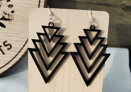 Wooden earring stand with geometric triangle earrings and pink flowers on a wooden background