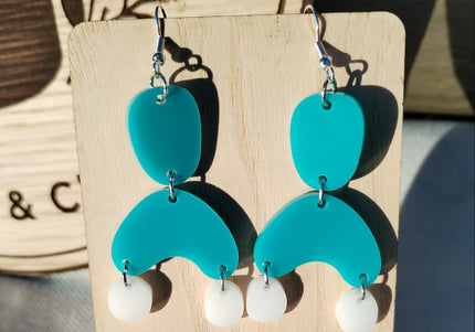 Turquoise and white earrings on a wooden stand with a floral background