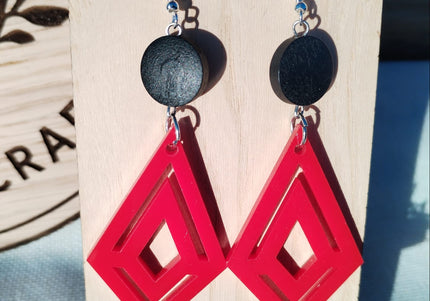 Red geometric earrings on a wooden stand with a natural background