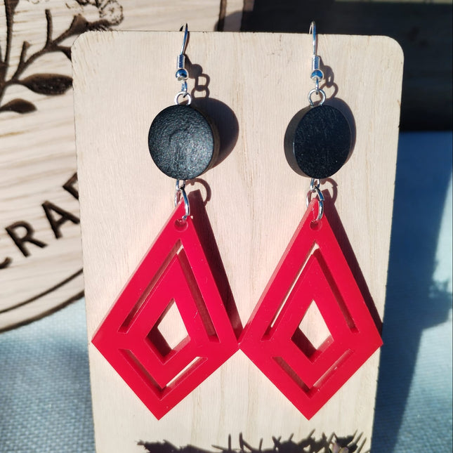 Red geometric earrings on a wooden stand with a natural background