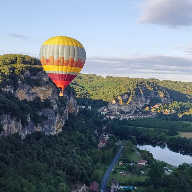 Hot air balloon over a scenic landscape with trees and a river.